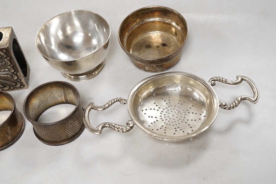 Sundry silver, consisting of - a modern tea strainer and stand, bu C.J. Vander Ltd, an egg cup, small goblet, three serviette rings, a stand and a match box case.